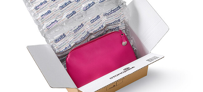 Ein Karton mit einer pinkfarbenen Tasche und bedruckten Luftpolstern