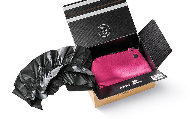 Ein Karton mit einer pinkfarbenen Tasche und schwarzen Papierpolstern
