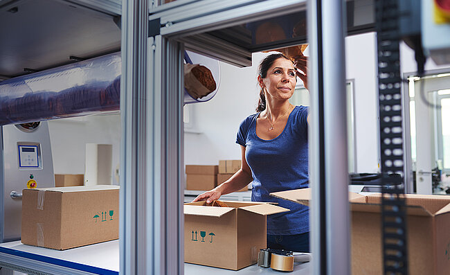 A woman packing products into a cardboard box at a packing station